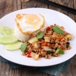 Thai stir-fry dish with rice and egg on rustic table setting, vibrant and appetizing.