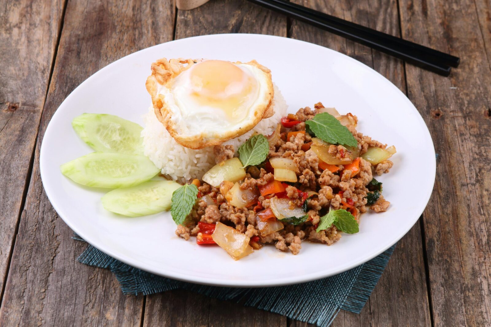 Thai stir-fry dish with rice and egg on rustic table setting, vibrant and appetizing.