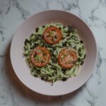 Colorful vegan meal featuring zucchini noodles, tomato slices, and seeds on a marble top.