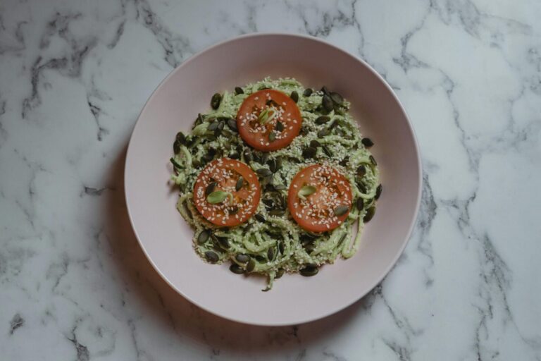 Colorful vegan meal featuring zucchini noodles, tomato slices, and seeds on a marble top.